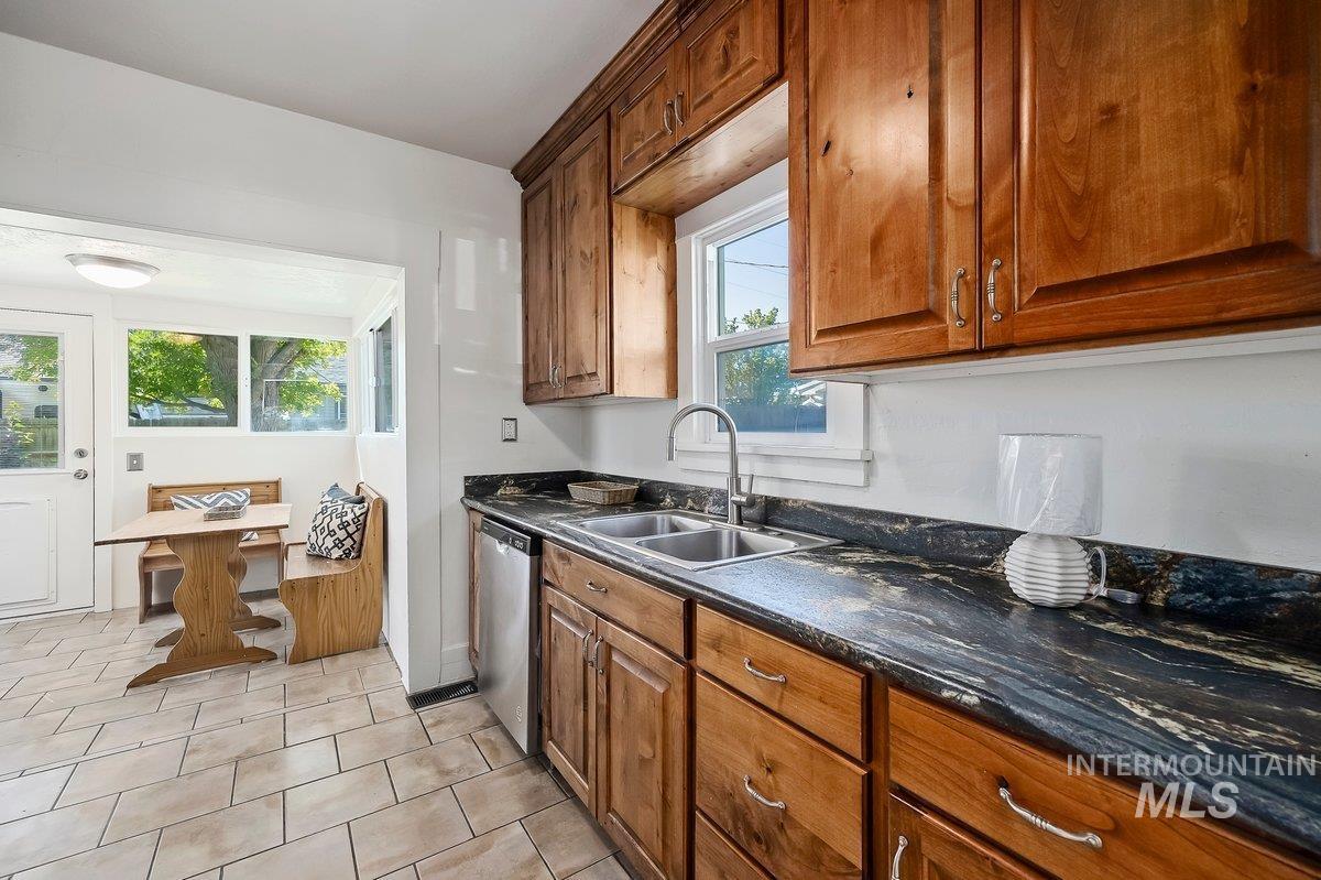 Kitchen featuring brown cabinetry, dishwasher, light tile patterned floors, and dark stone countertops