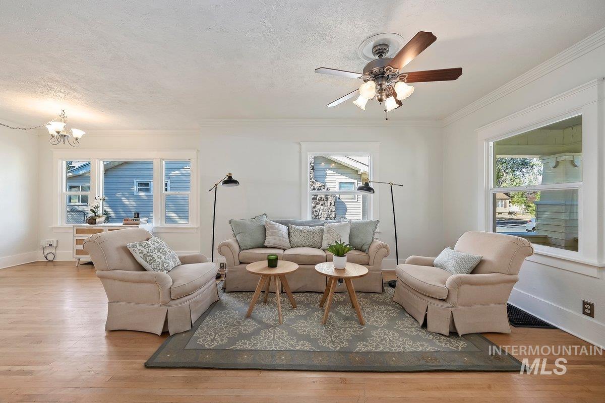 Living area featuring light wood-type flooring, crown molding, a textured ceiling, a chandelier, and ceiling fan