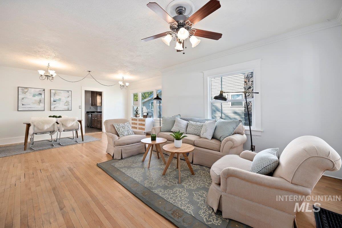 Living area featuring crown molding, light wood-style flooring, a chandelier, and ceiling fan