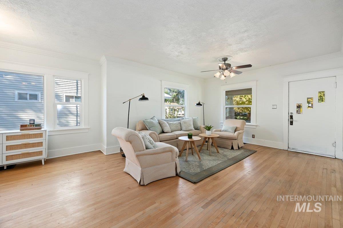 Living area featuring light wood-style floors, a textured ceiling, ornamental molding, and ceiling fan