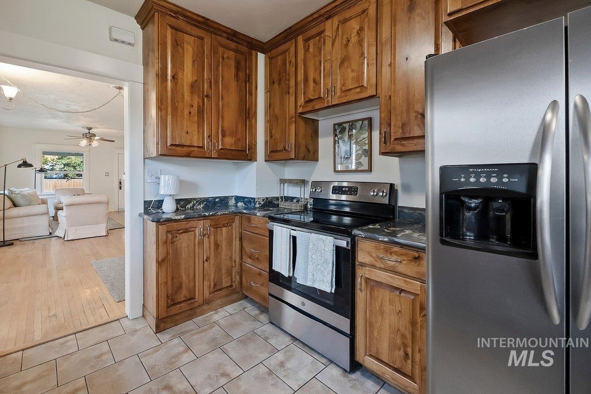 Kitchen featuring stainless steel appliances, dark stone counters, a ceiling fan, and brown cabinets