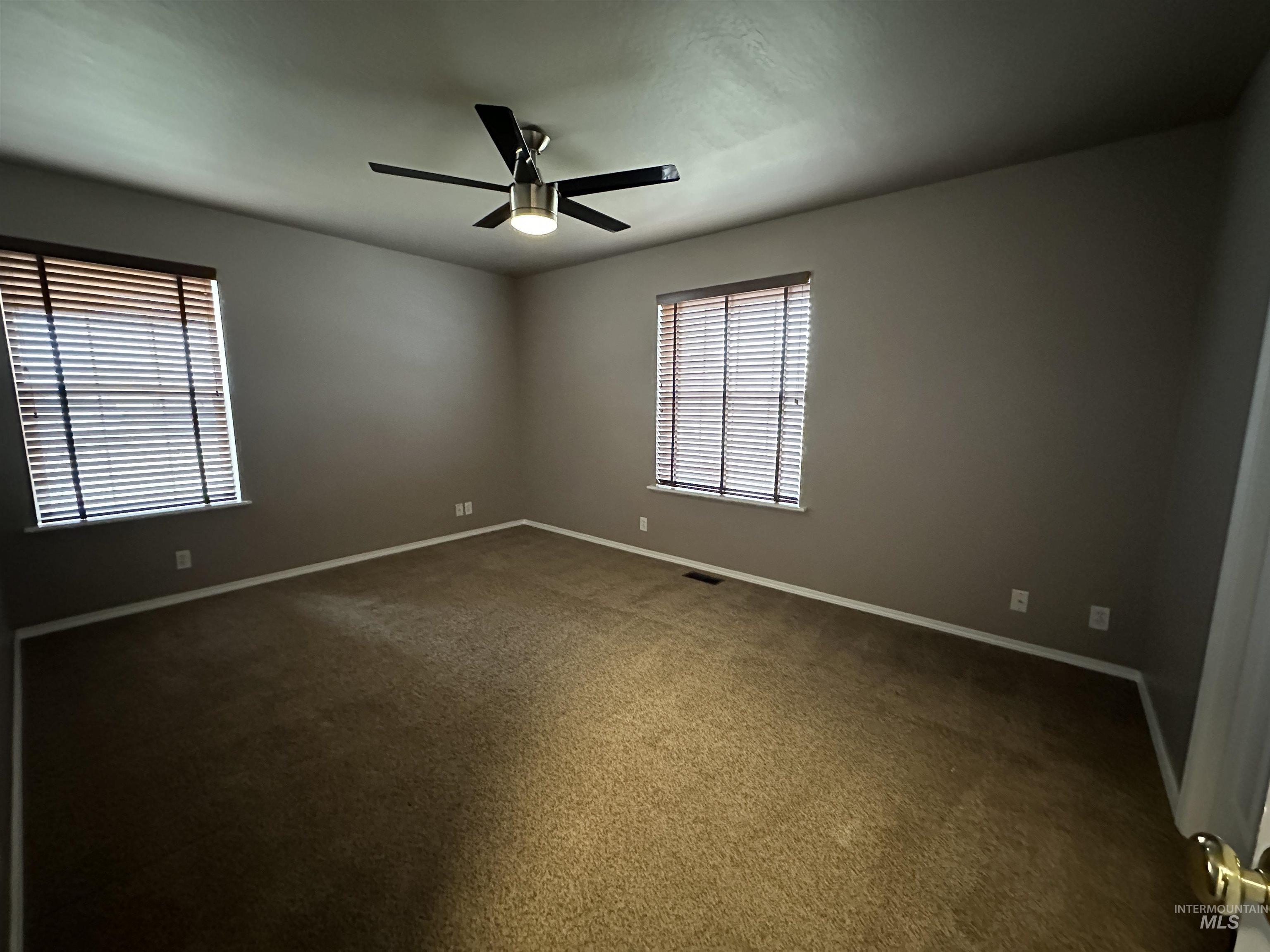 Unfurnished room featuring dark colored carpet and a ceiling fan