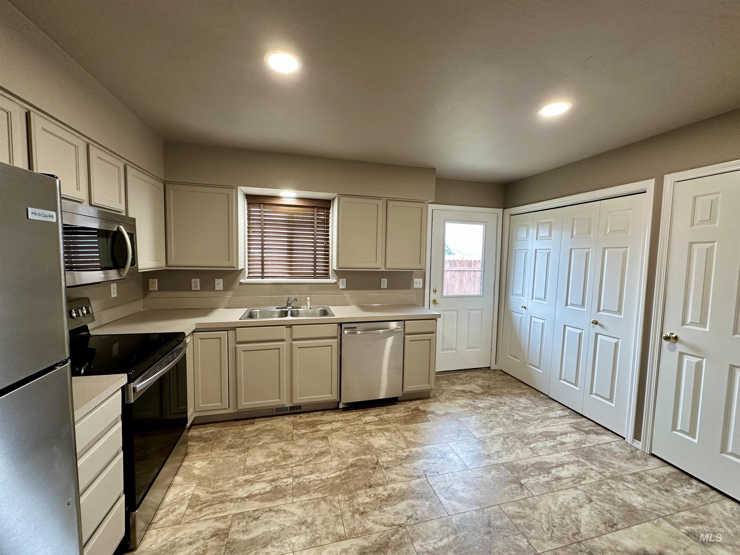 Kitchen with appliances with stainless steel finishes, light countertops, recessed lighting, and stone finish flooring