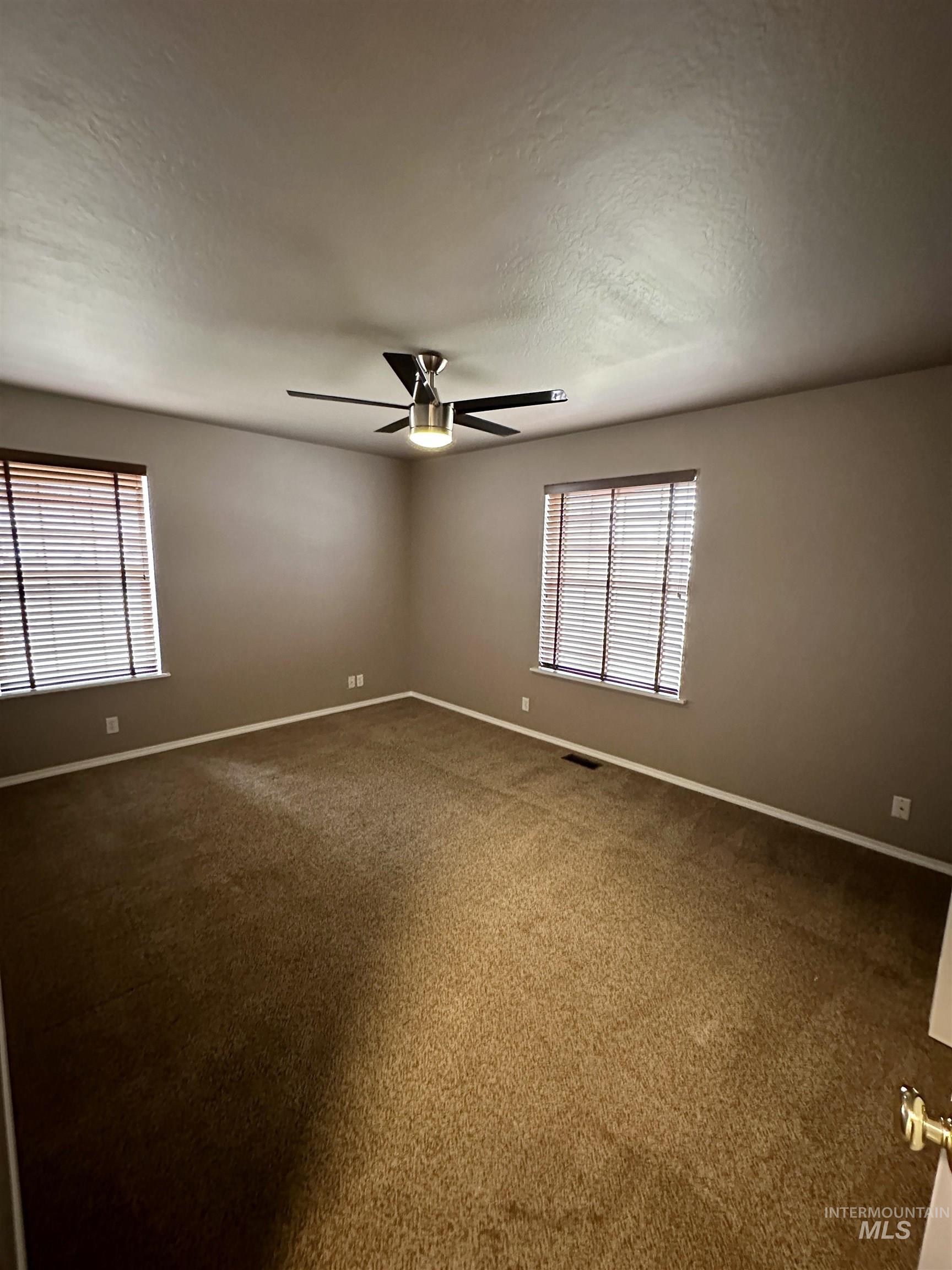 Spare room featuring dark carpet, healthy amount of natural light, a textured ceiling, and ceiling fan