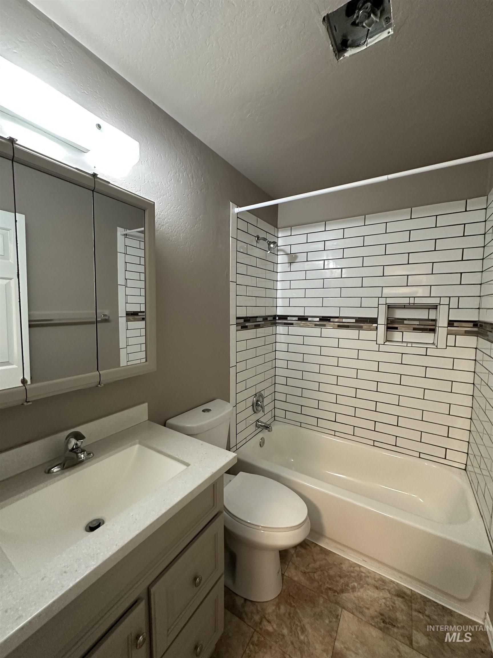 Bathroom with shower / bathtub combination, vanity, a textured wall, and a textured ceiling