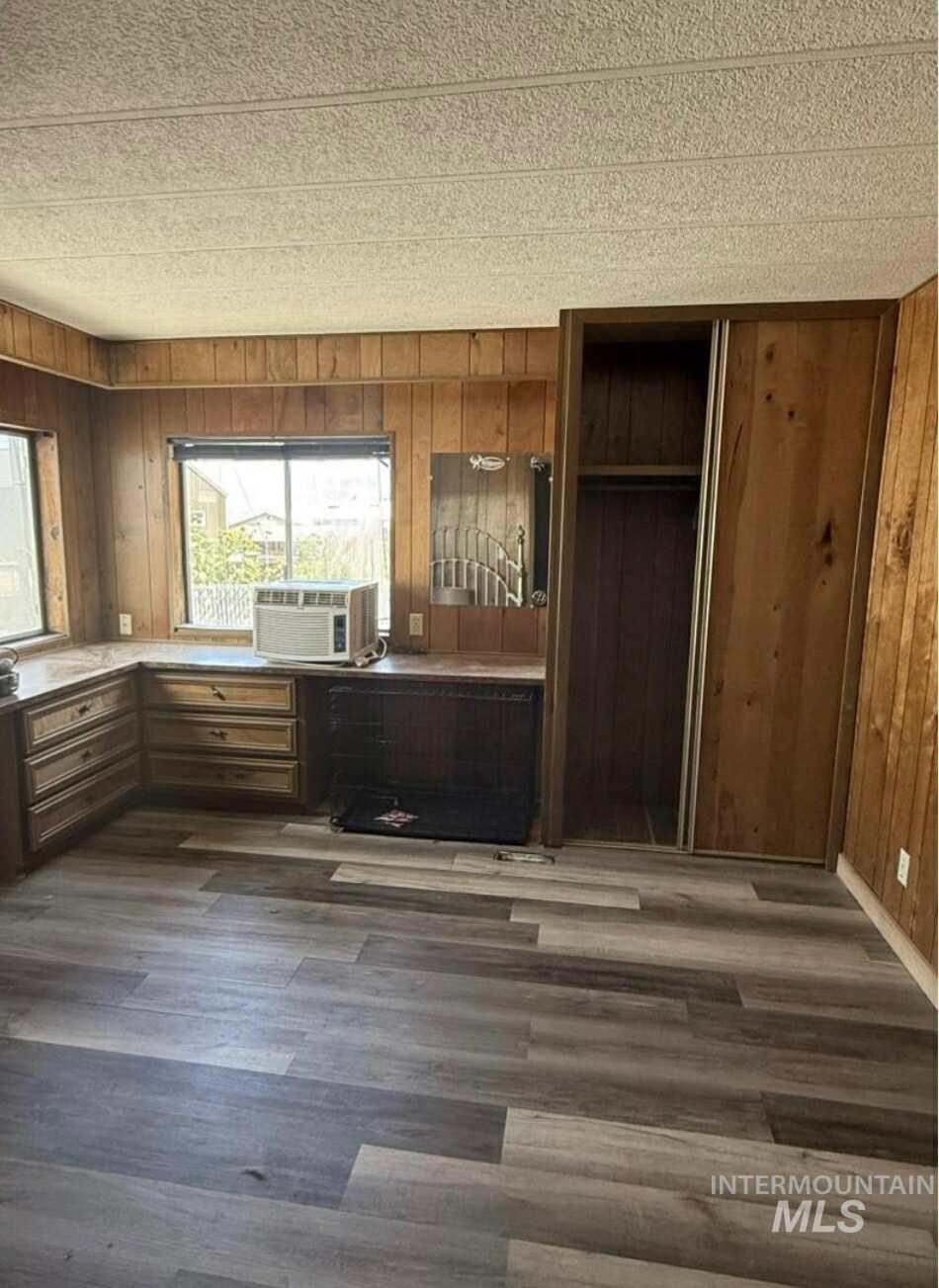Primary bedroom with wooden walls, dark wood-style floors, cooling unit, and a textured ceiling