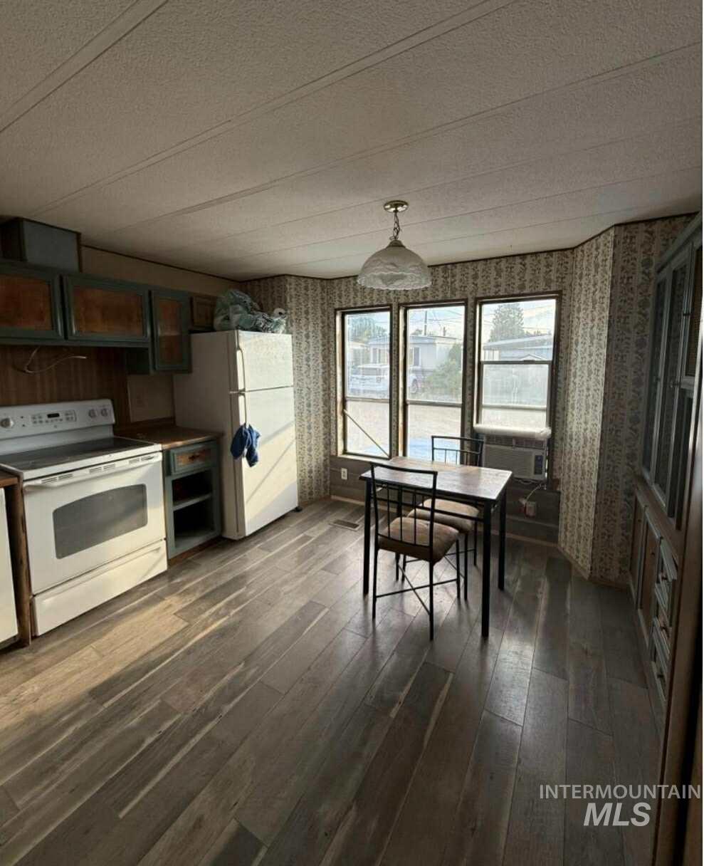 Kitchen with wallpapered walls, white appliances, decorative light fixtures, dark wood-type flooring, and a textured ceiling