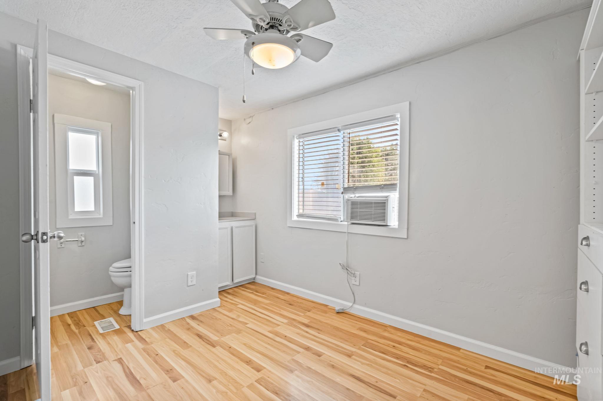 Unfurnished bedroom with light wood-type flooring, ceiling fan, ensuite bathroom, a textured ceiling, and cooling unit