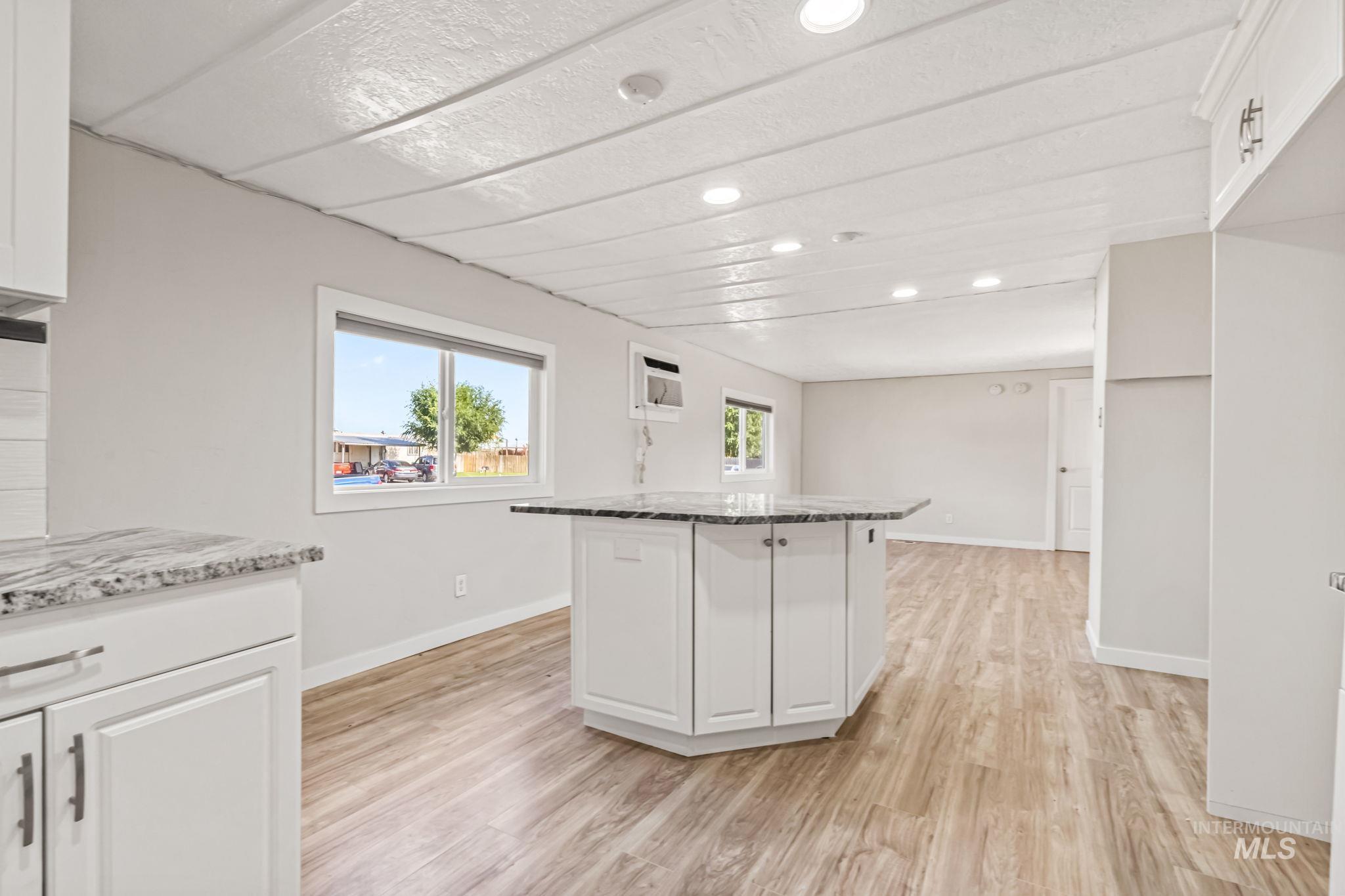 Kitchen with white cabinets, recessed lighting, light wood-style floors, light stone counters, and a center island