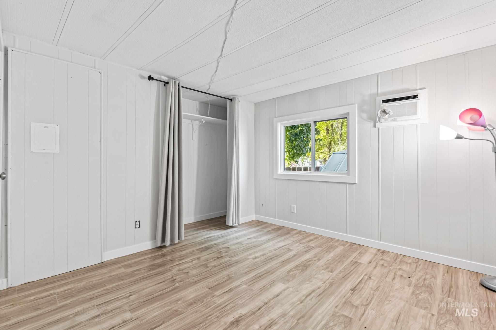 Unfurnished bedroom with light wood-style flooring, wooden walls, and a wall unit AC
