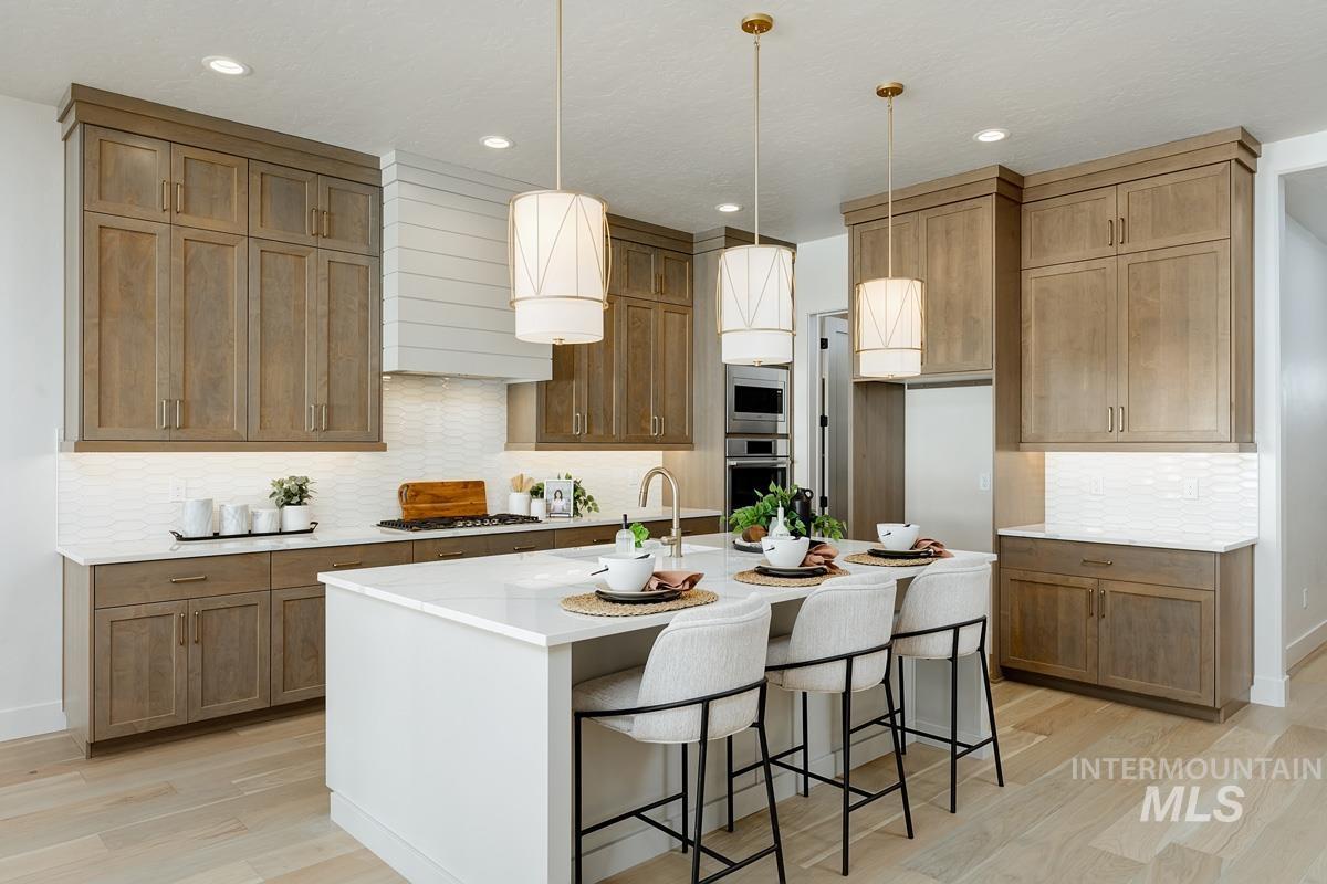 Kitchen featuring decorative backsplash, a breakfast bar, pendant lighting, light wood-type flooring, and light stone countertops