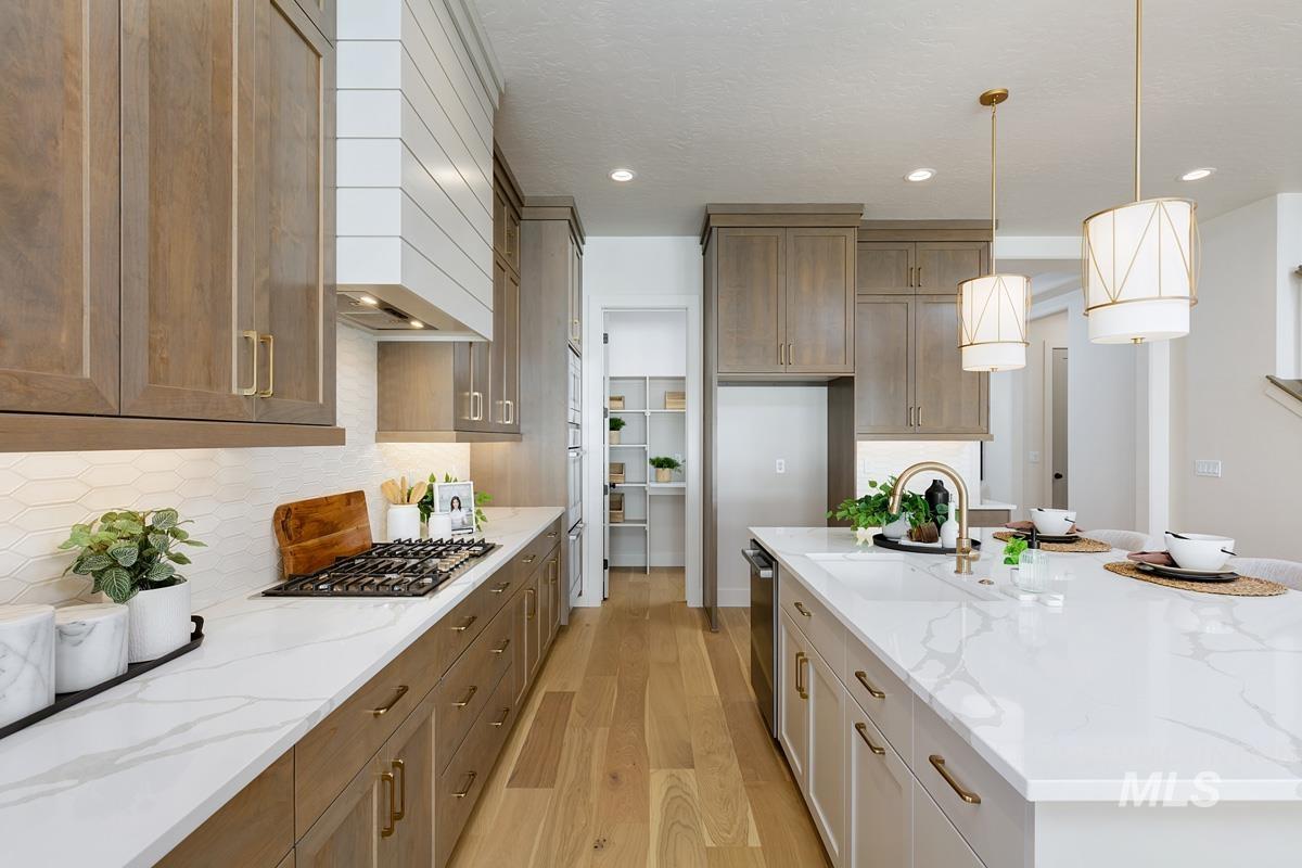 Kitchen featuring light stone countertops, light wood-style flooring, decorative light fixtures, a large island, and decorative backsplash