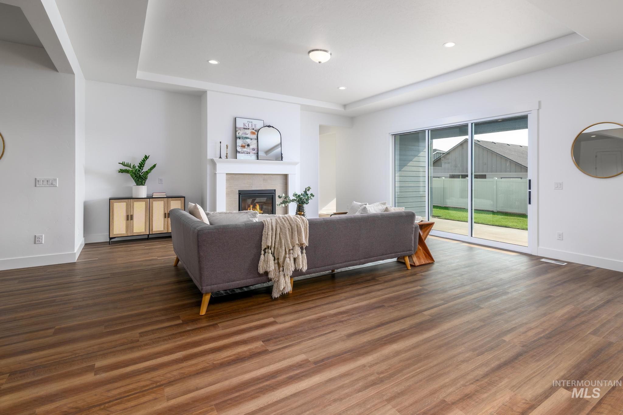 Living area featuring a tray ceiling, a glass covered fireplace, dark wood-style flooring, and recessed lighting