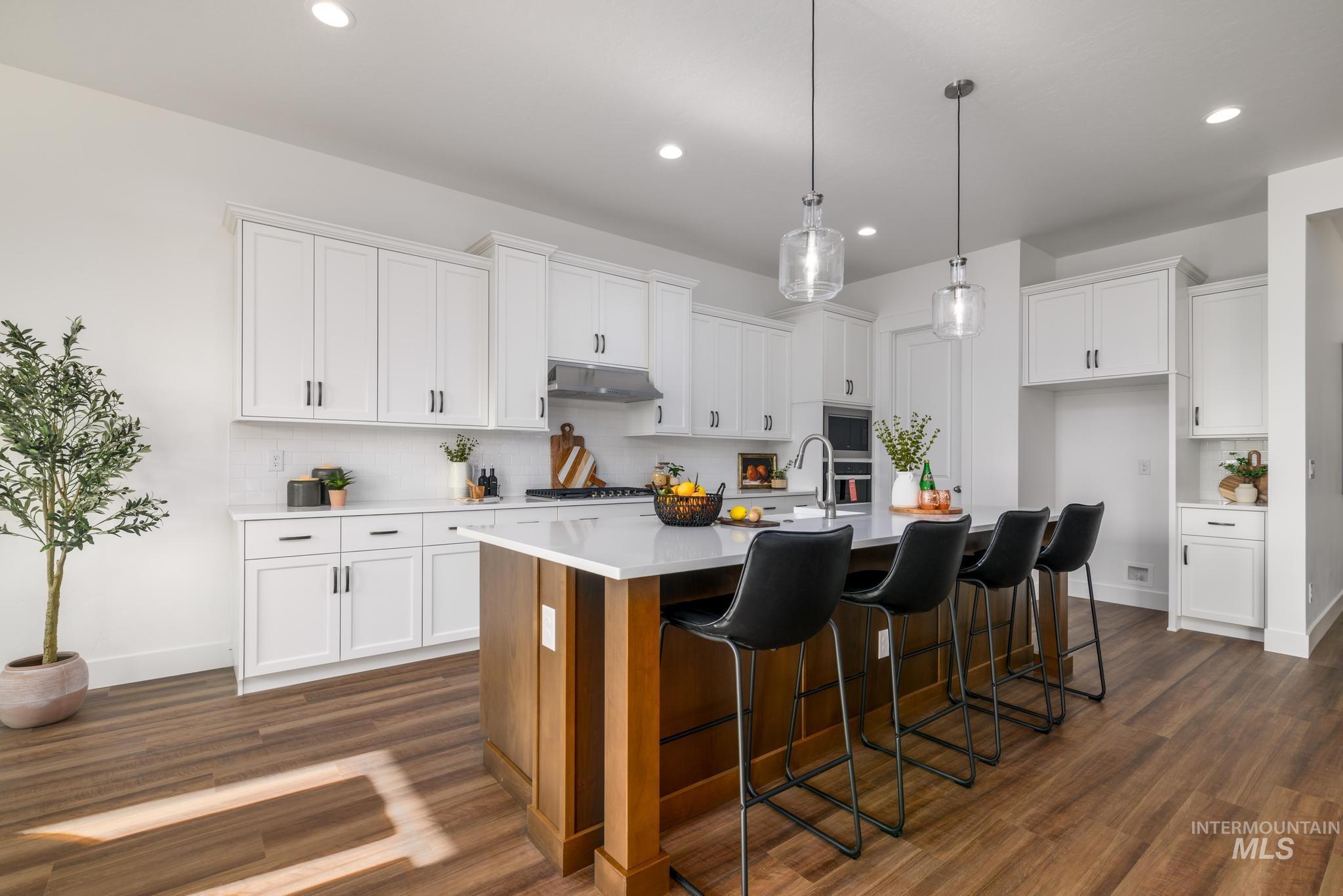 Kitchen featuring a kitchen bar, a center island with sink, white cabinetry, tasteful backsplash, and decorative light fixtures