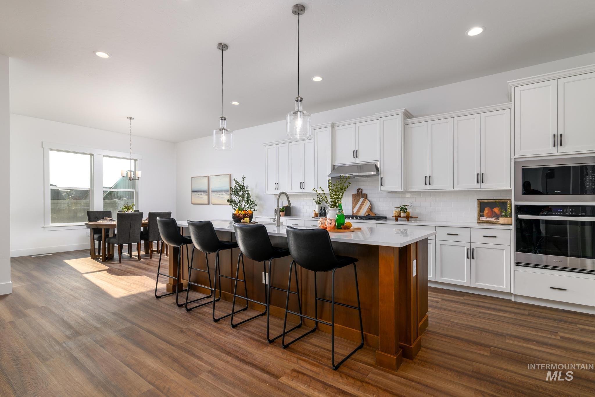 Kitchen featuring decorative backsplash, pendant lighting, a kitchen bar, white cabinetry, and recessed lighting