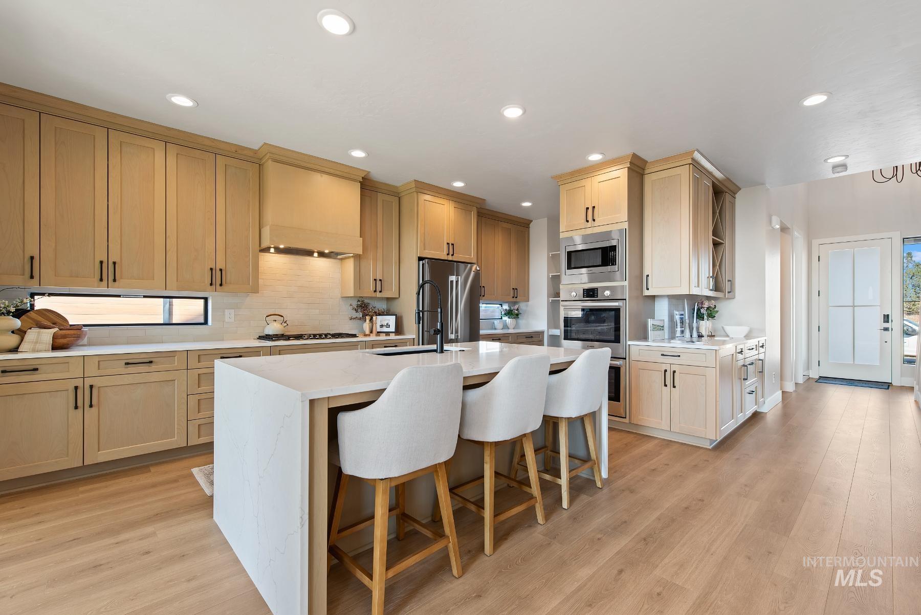 Kitchen featuring a breakfast bar area, light stone countertops, light wood-style floors, backsplash, and stainless steel appliances
