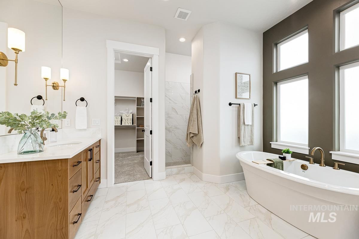 Full bath featuring vanity, a marble finish shower, a spacious closet, a freestanding bath, and light marble finish floors