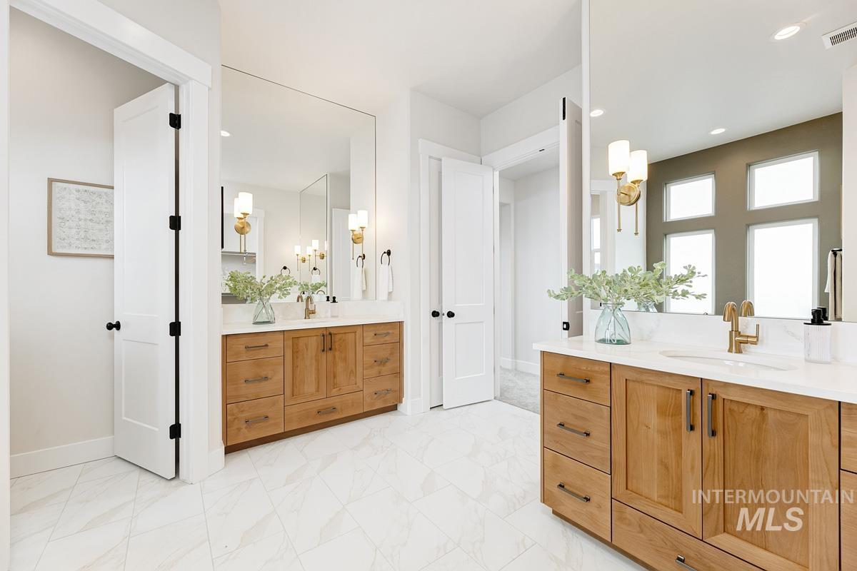Full bathroom featuring two vanities, light marble finish flooring, and recessed lighting