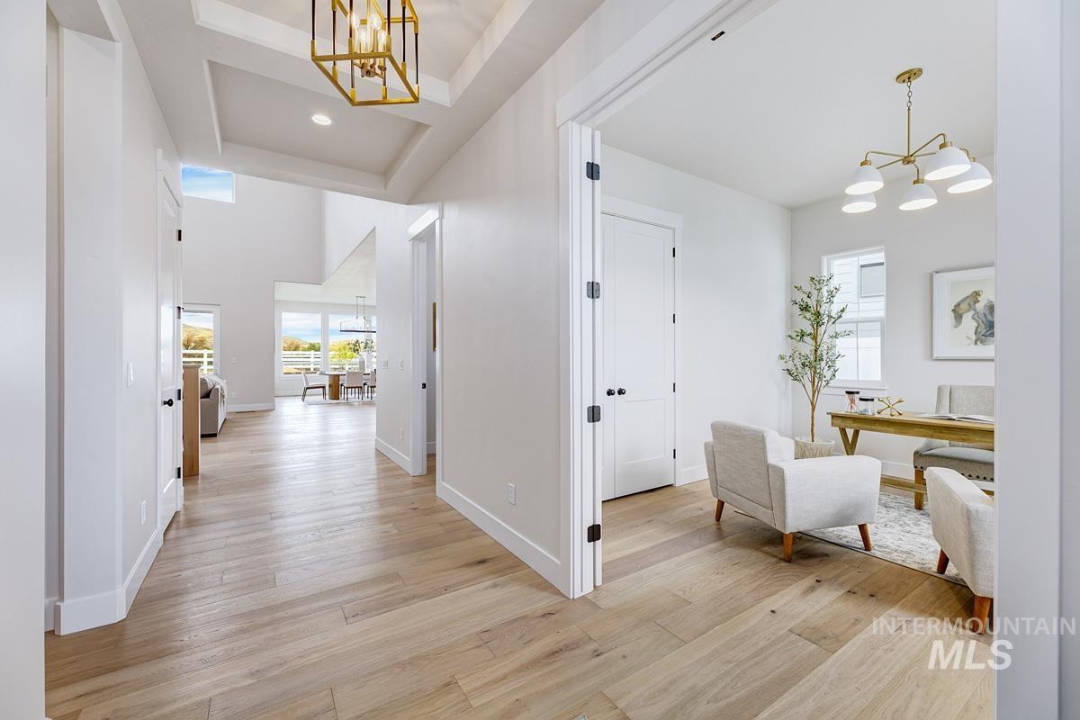 Hallway featuring a chandelier, light wood-style floors, a desk, and a tray ceiling