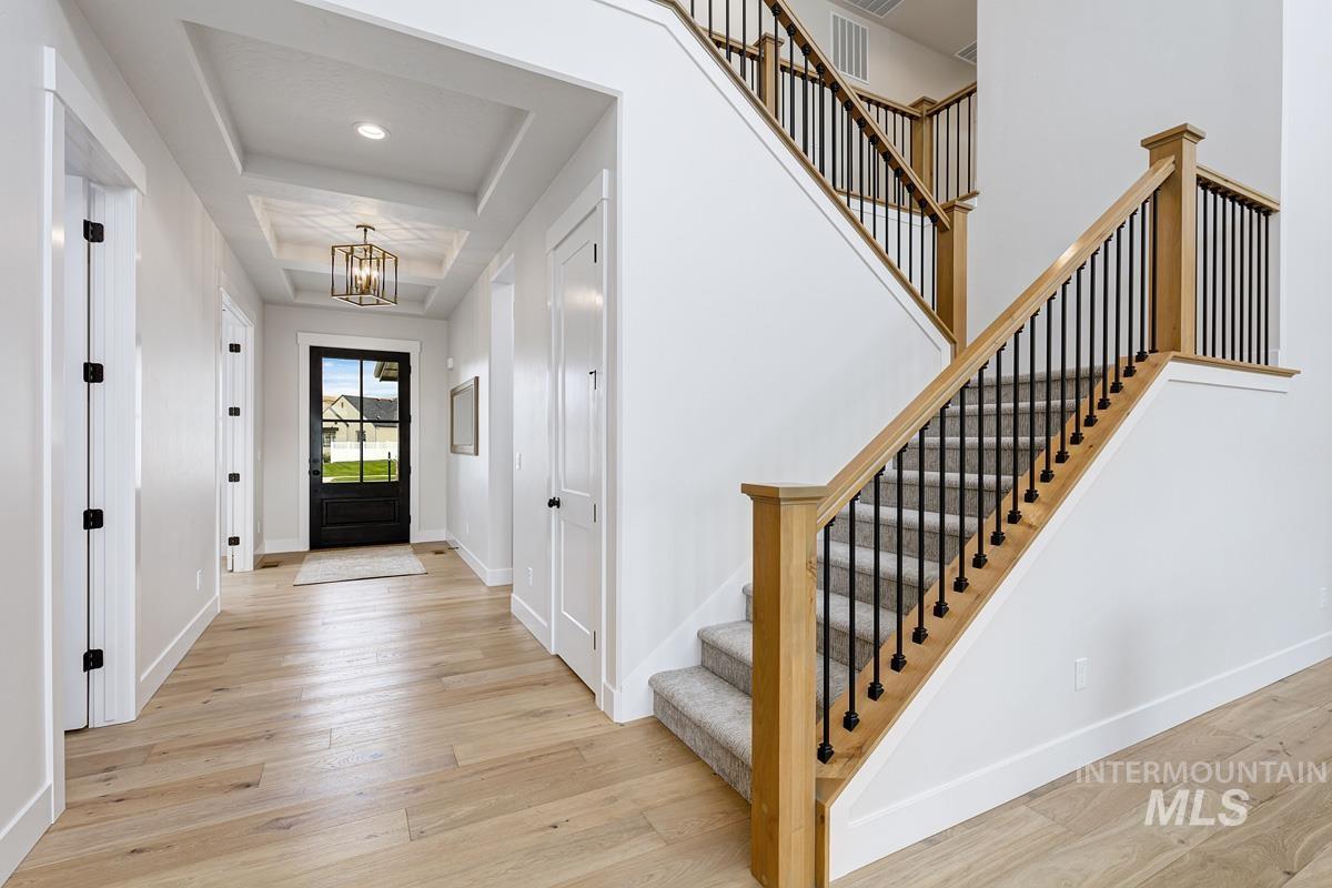 Entrance foyer with light wood-style flooring, a chandelier, a raised ceiling, and stairway
