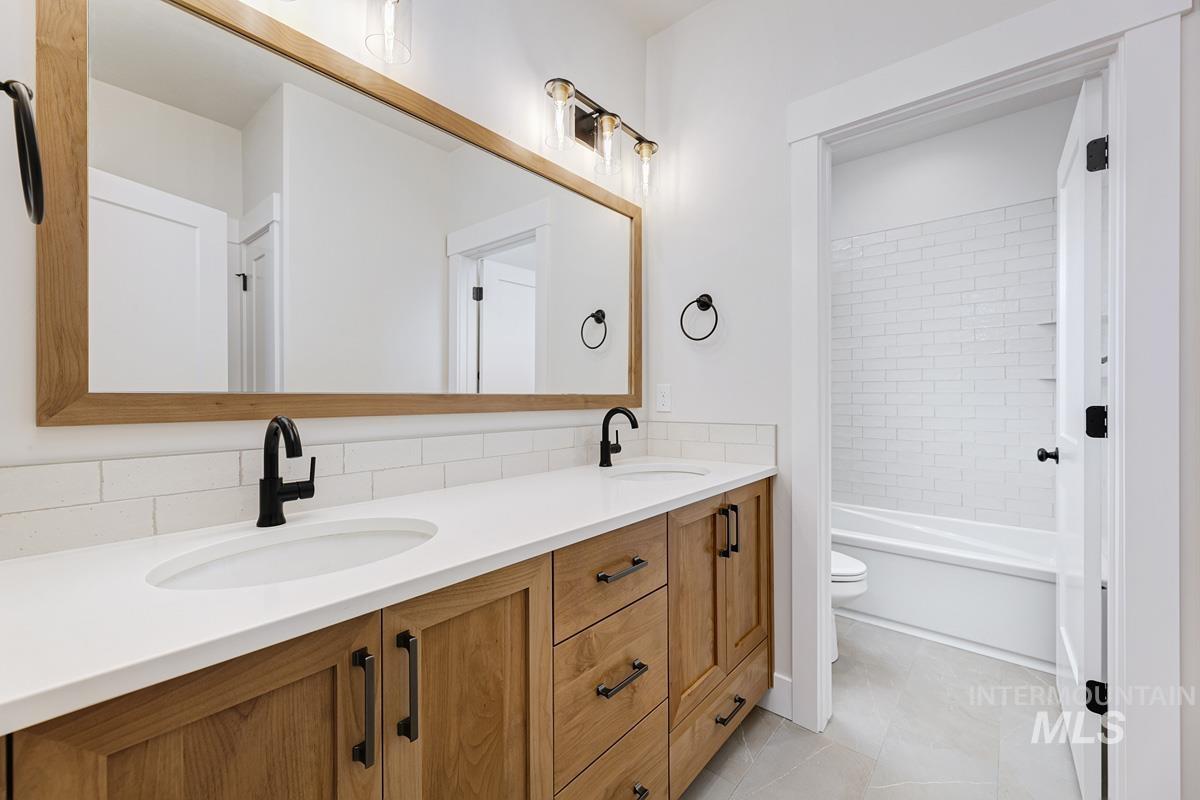 Bathroom featuring double vanity, shower / washtub combination, light tile patterned floors, and backsplash