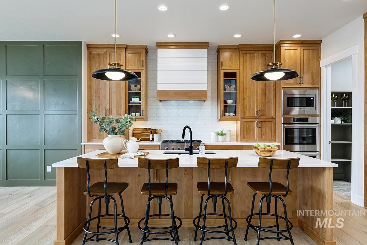 Kitchen featuring decorative backsplash, brown cabinetry, a kitchen island with sink, stainless steel appliances, and a kitchen bar
