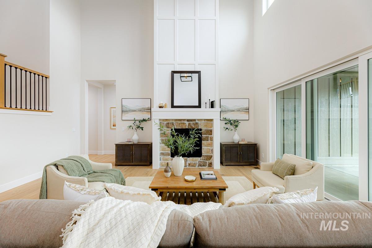 Living room featuring a towering ceiling, wood finished floors, and a stone fireplace