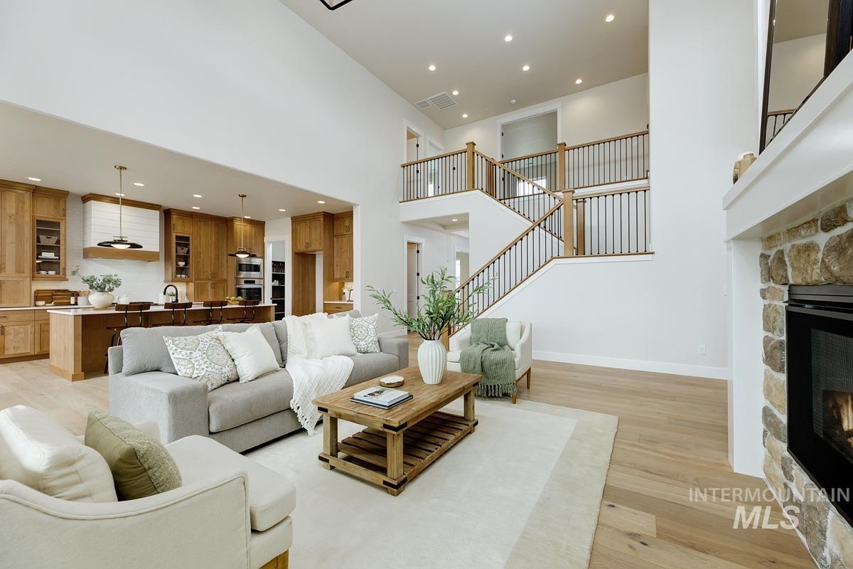 Living area featuring a high ceiling, light wood finished floors, a stone fireplace, recessed lighting, and stairway