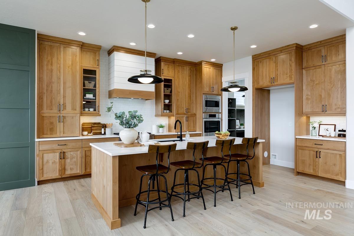 Kitchen featuring tasteful backsplash, a kitchen breakfast bar, light wood-style flooring, an island with sink, and pendant lighting