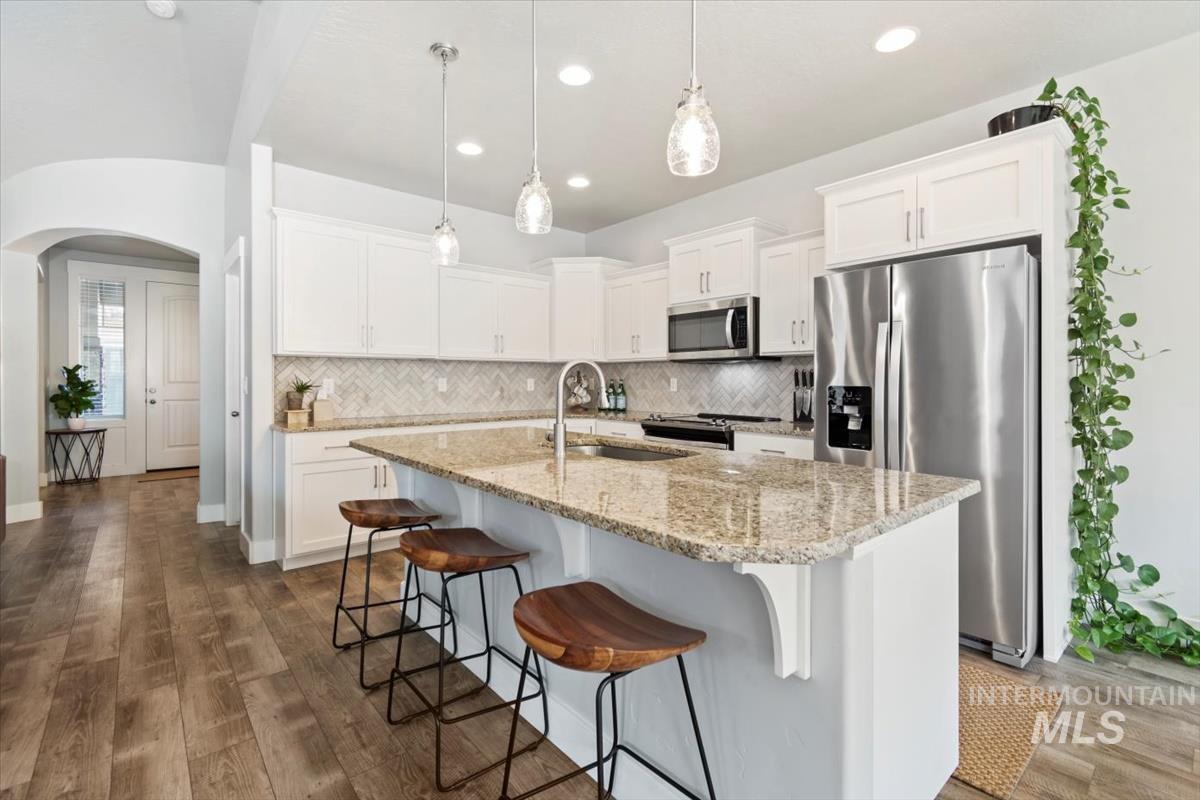 Kitchen featuring arched walkways, stainless steel appliances, a breakfast bar, a kitchen island with sink, and light stone countertops