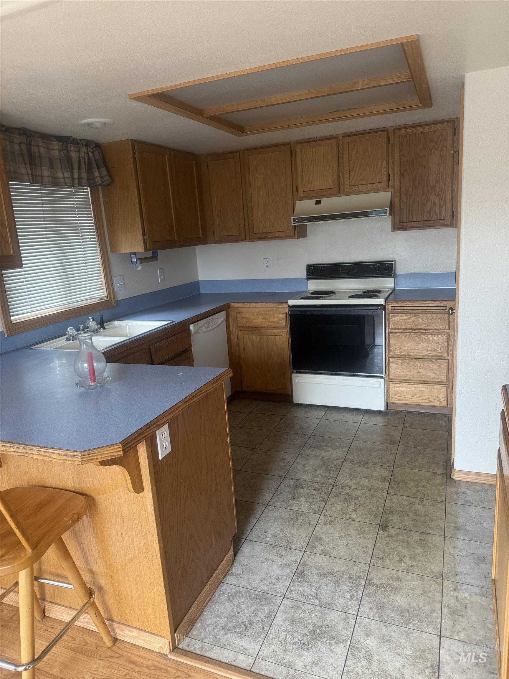 Kitchen featuring electric stove, a peninsula, a breakfast bar, brown cabinetry, and under cabinet range hood
