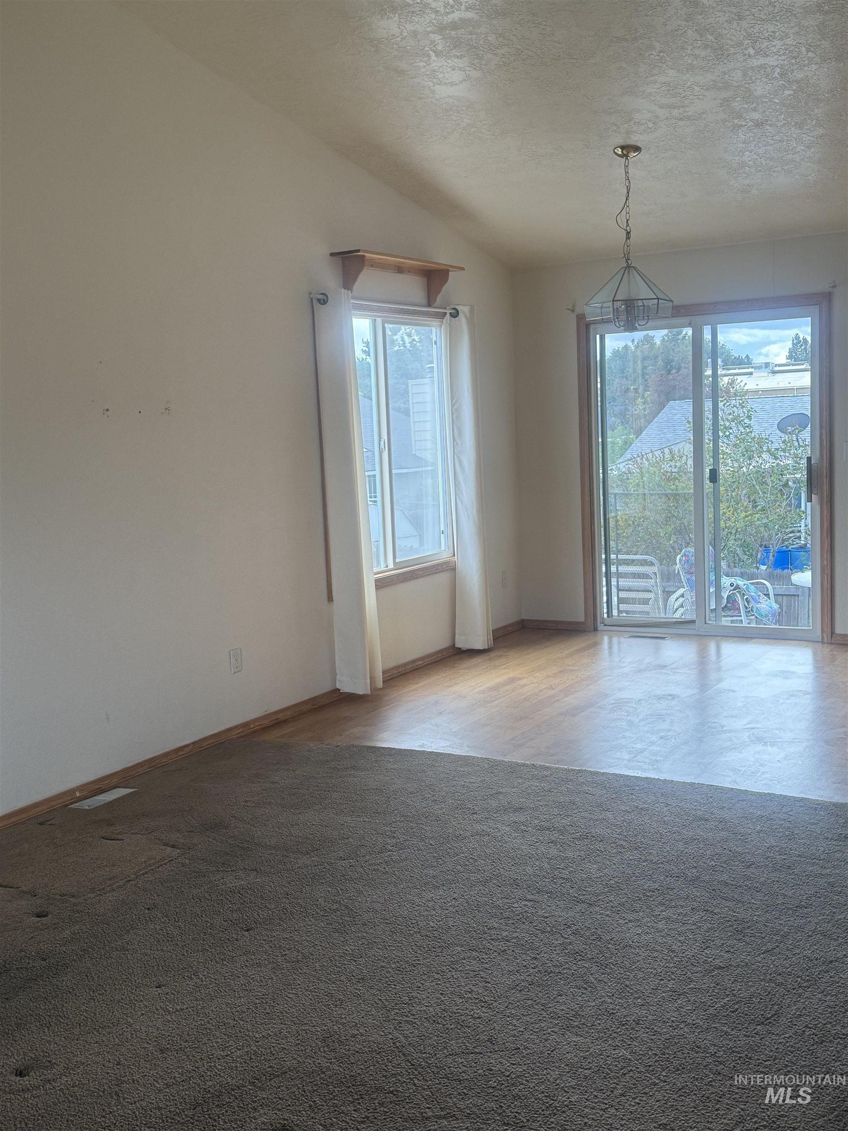 Unfurnished room with healthy amount of natural light, a textured ceiling, and light carpet