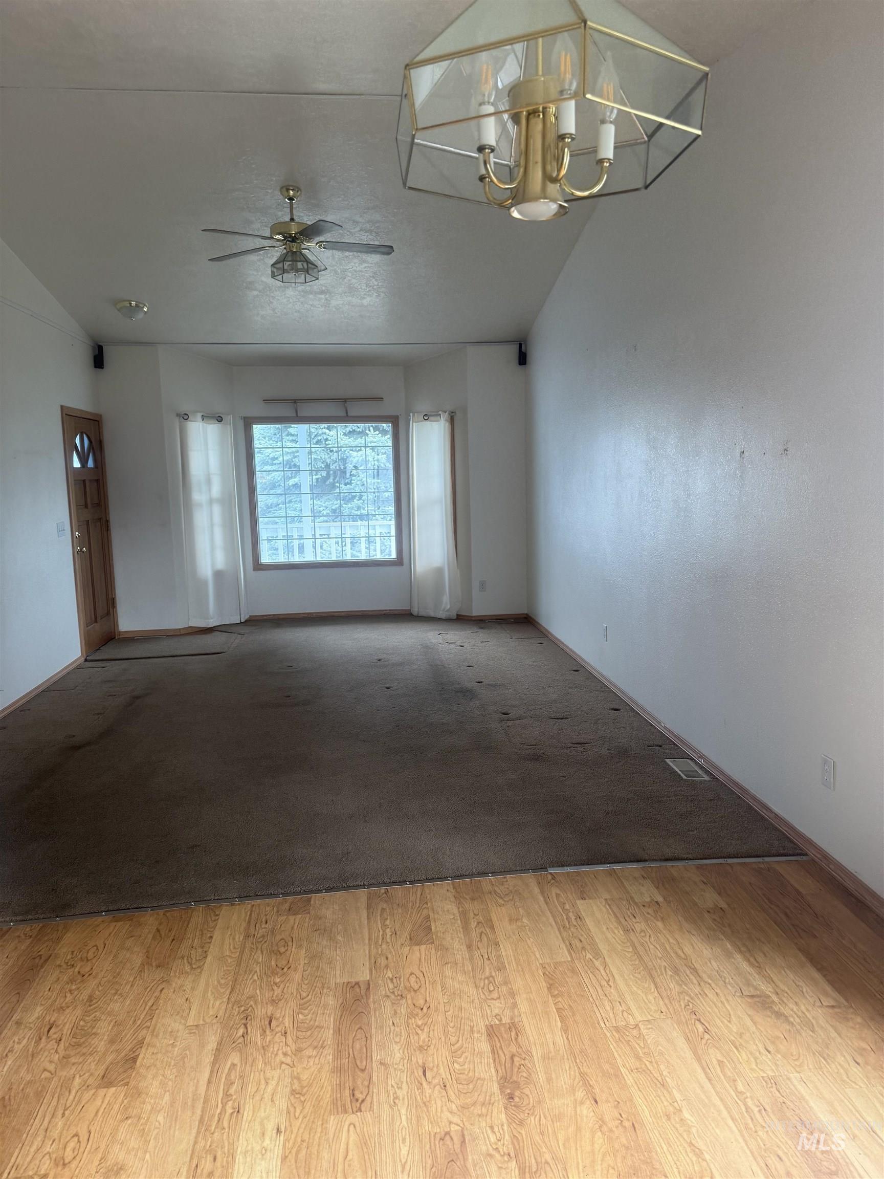 Unfurnished room with lofted ceiling, a chandelier, light wood-style flooring, and a ceiling fan