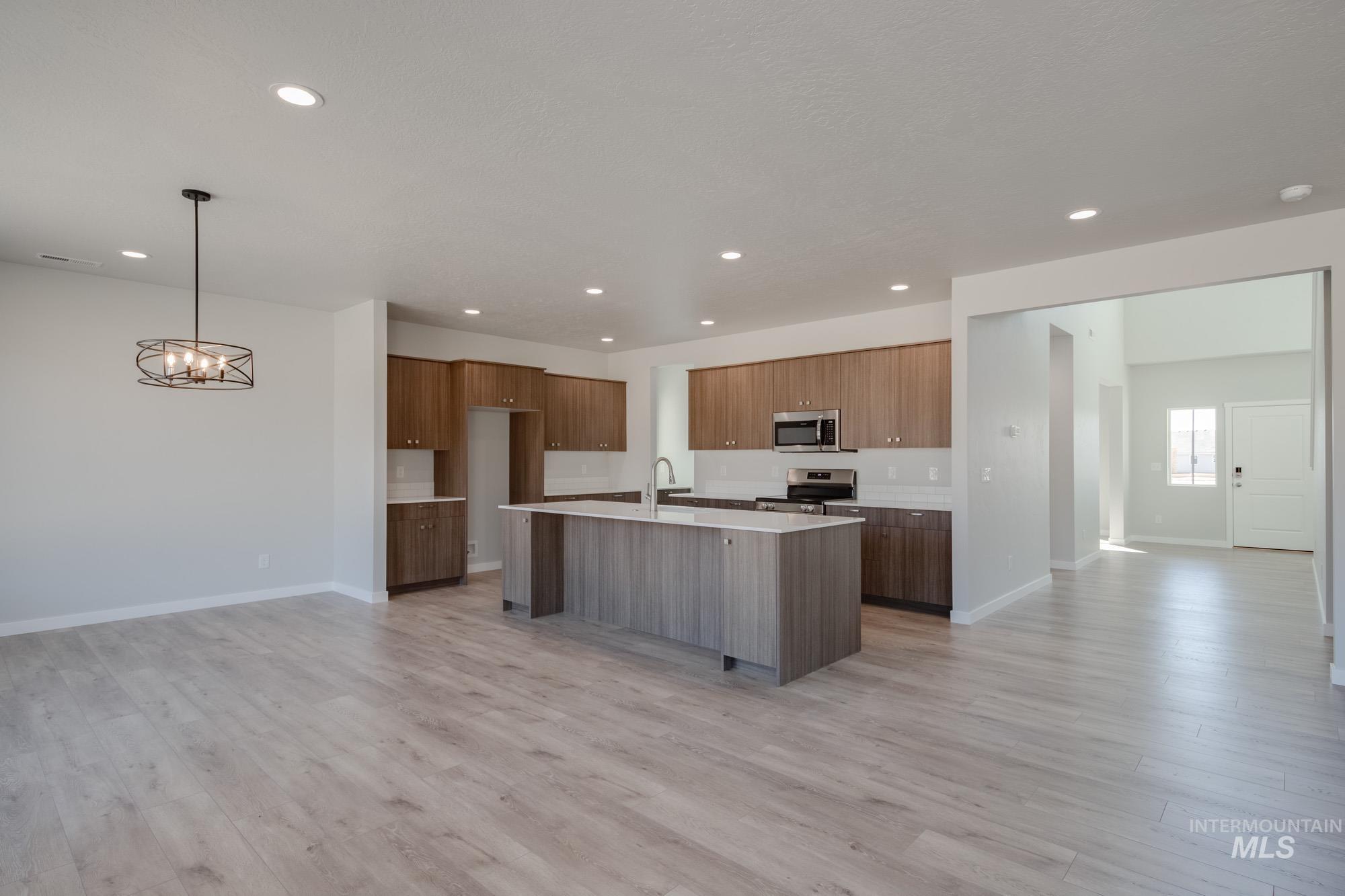 Kitchen with open floor plan, an island with sink, light wood finished floors, appliances with stainless steel finishes, and recessed lighting