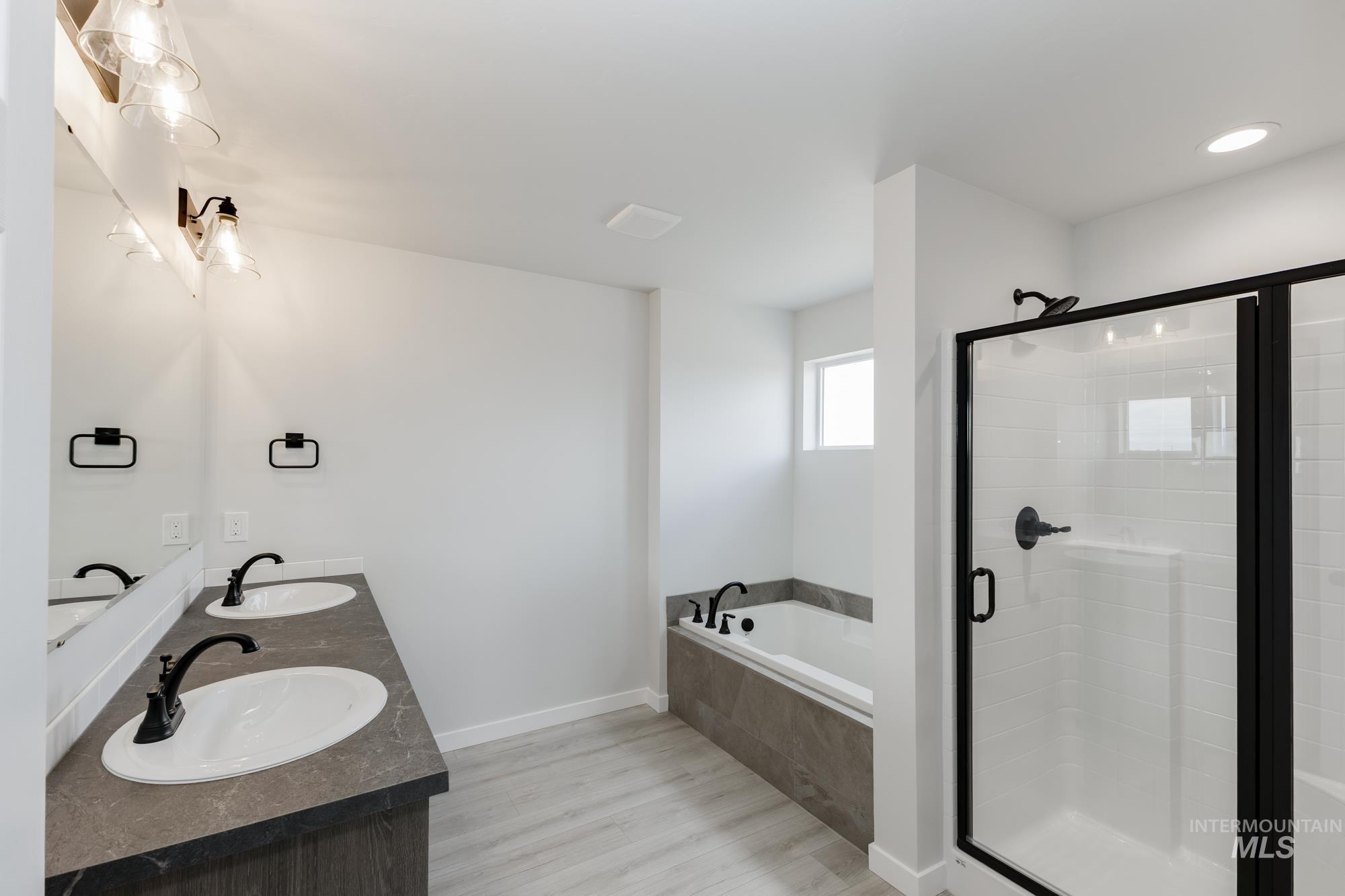 Bathroom featuring a stall shower, light wood finished floors, a bath, and double vanity