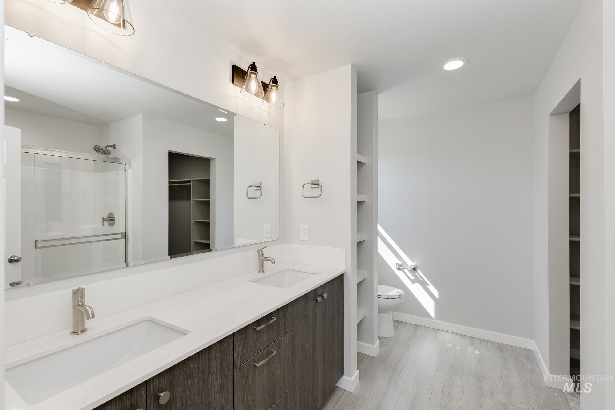 Full bathroom featuring a walk in closet, a shower stall, double vanity, recessed lighting, and light wood-style flooring