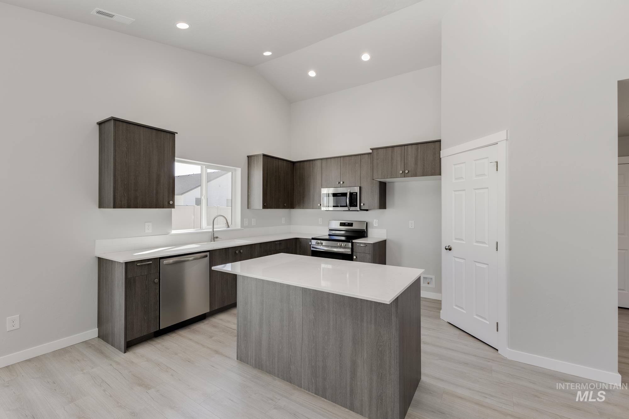 Kitchen with modern cabinets, dark brown cabinetry, high vaulted ceiling, stainless steel appliances, and a kitchen island