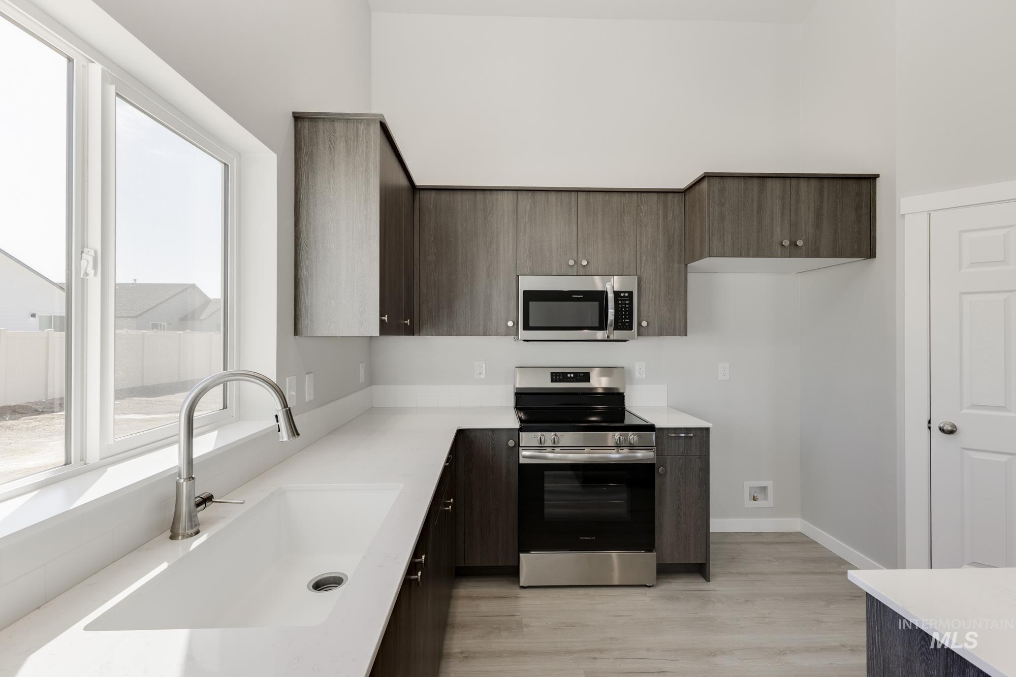 Kitchen featuring dark brown cabinetry, appliances with stainless steel finishes, light wood-style flooring, light stone countertops, and modern cabinets