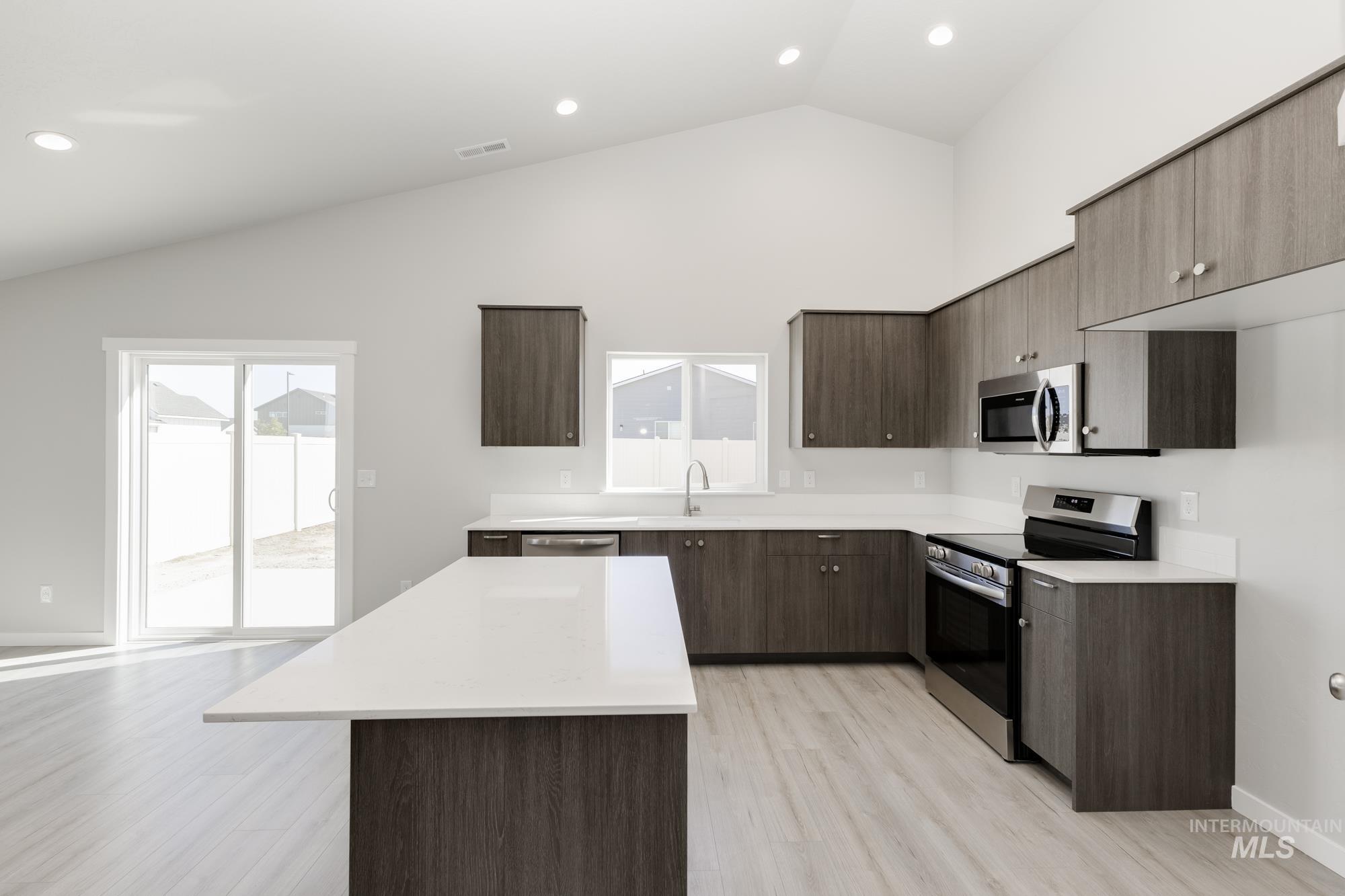 Kitchen with appliances with stainless steel finishes, a kitchen island, modern cabinets, light wood finished floors, and dark brown cabinetry