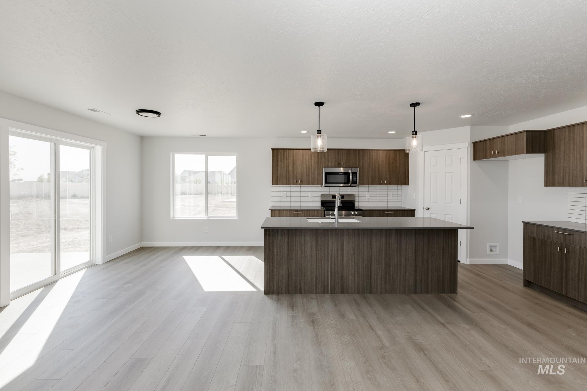 Kitchen with modern cabinets, tasteful backsplash, decorative light fixtures, an island with sink, and light wood-style flooring