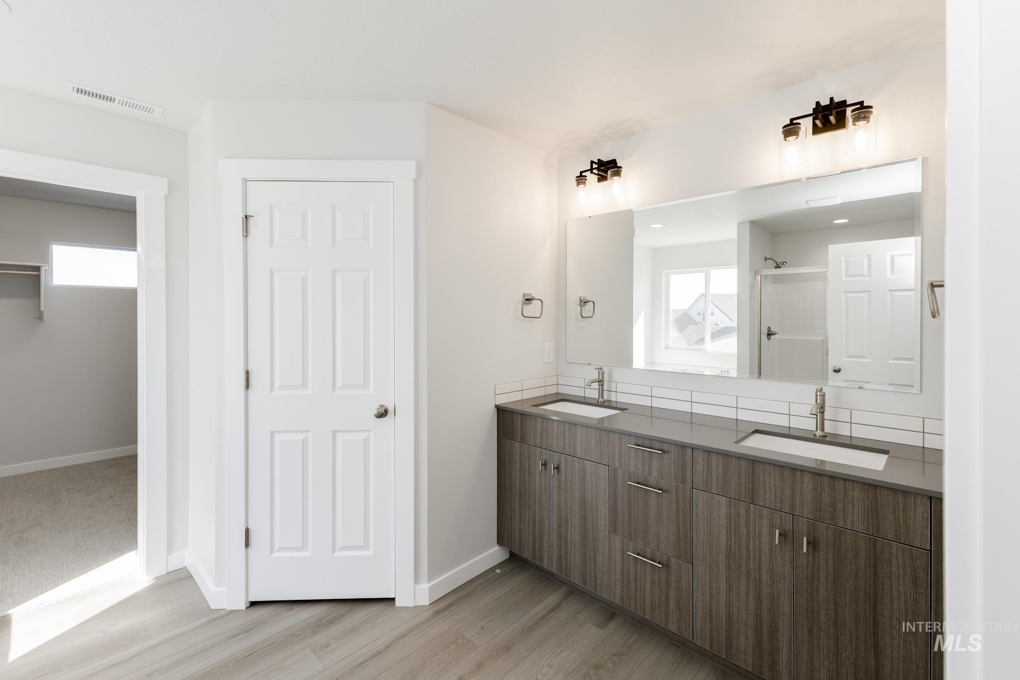 Bathroom with double vanity, a stall shower, light wood finished floors, and a walk in closet