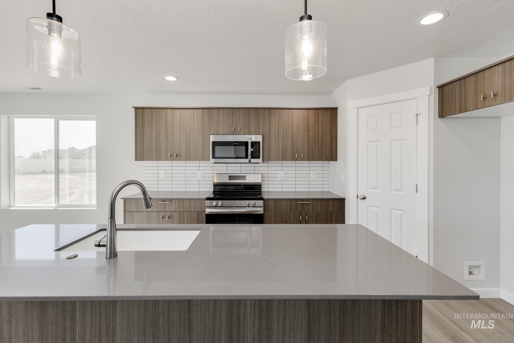 Kitchen featuring modern cabinets, stainless steel appliances, decorative backsplash, light stone counters, and pendant lighting