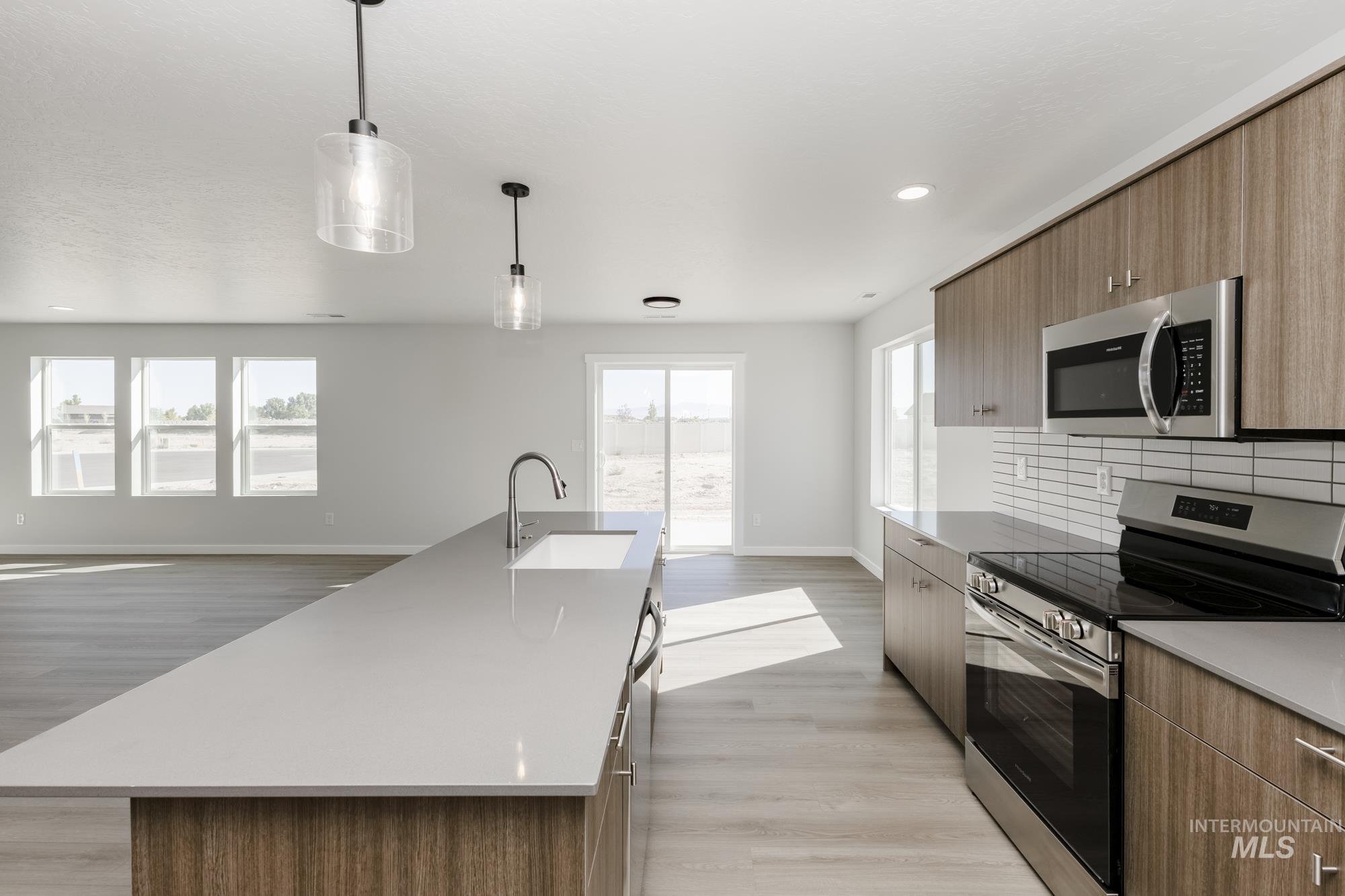 Kitchen featuring appliances with stainless steel finishes, modern cabinets, an island with sink, light wood finished floors, and pendant lighting
