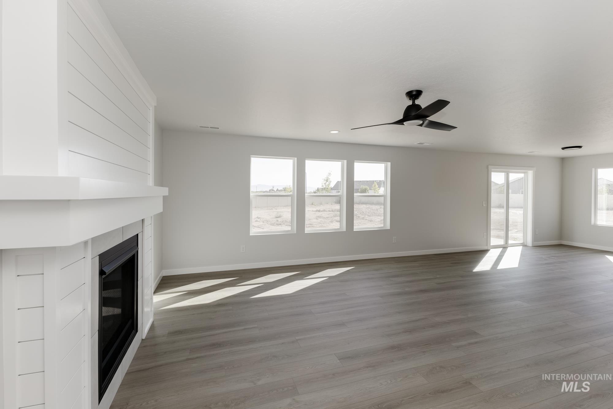 Unfurnished living room featuring light wood-style floors, plenty of natural light, a fireplace, and a ceiling fan