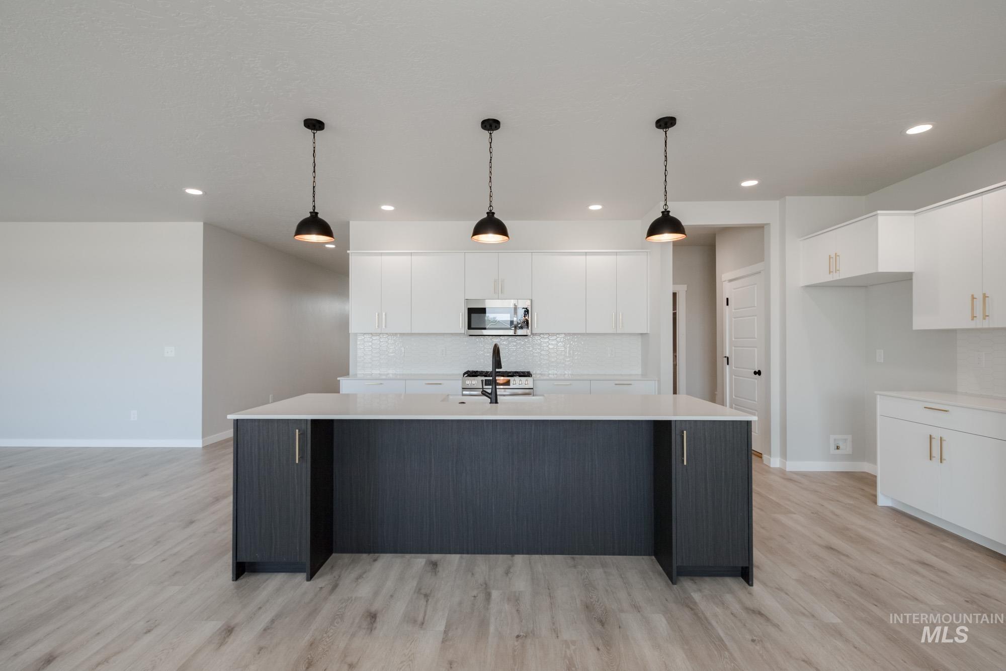 Kitchen with decorative backsplash, white cabinetry, a kitchen island with sink, pendant lighting, and light wood-style floors