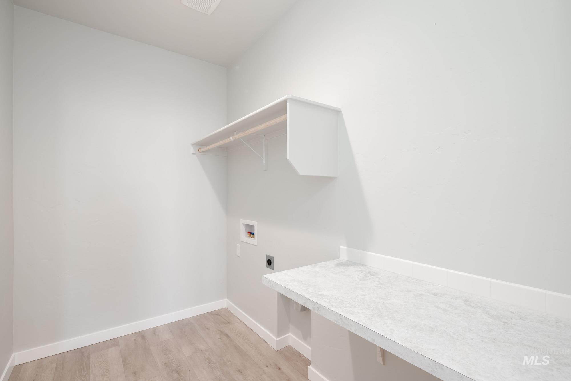 Laundry area with hookup for an electric dryer, light wood-style floors, and washer hookup