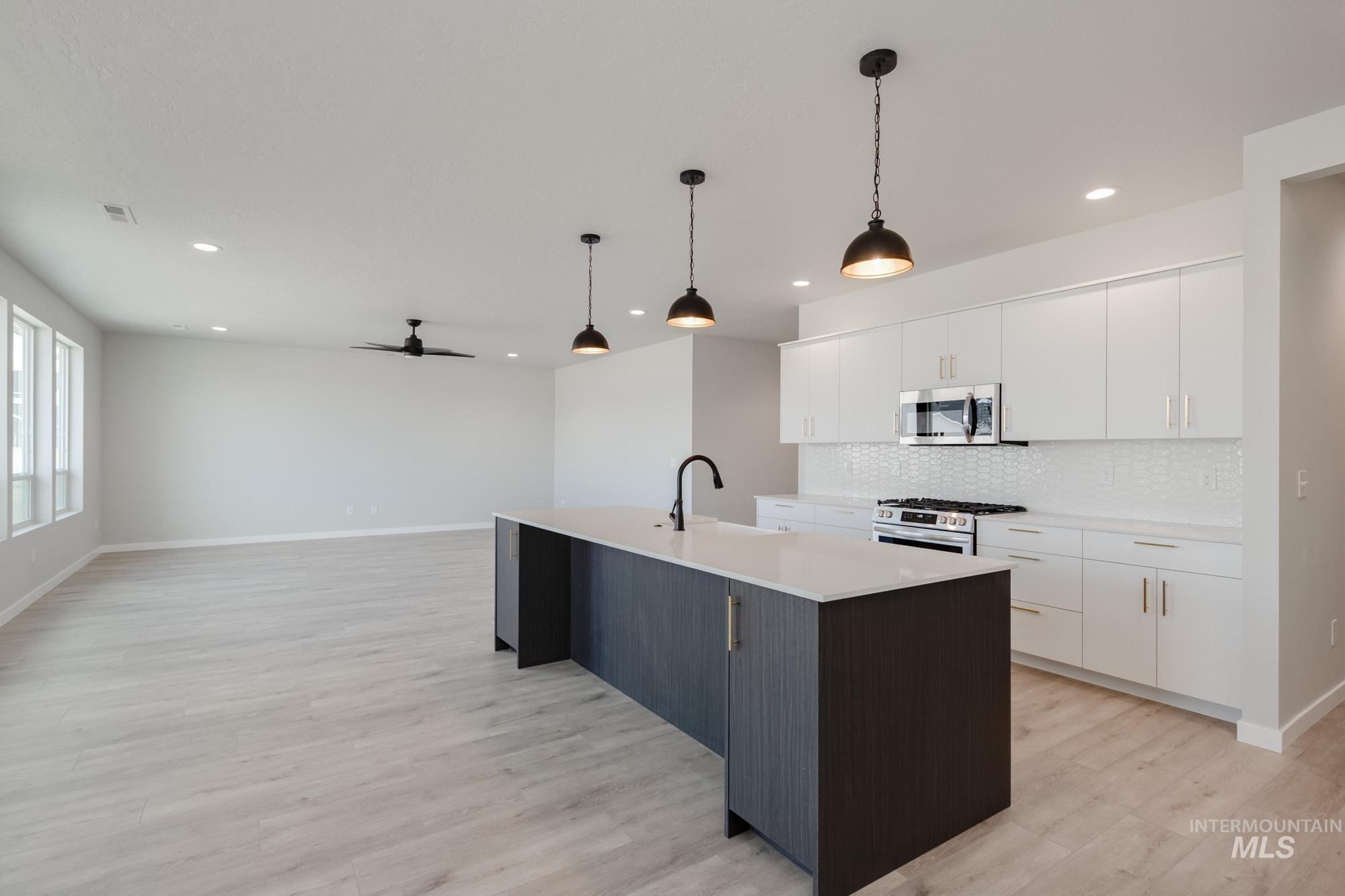 Kitchen featuring white cabinetry, ceiling fan, an island with sink, decorative light fixtures, and recessed lighting