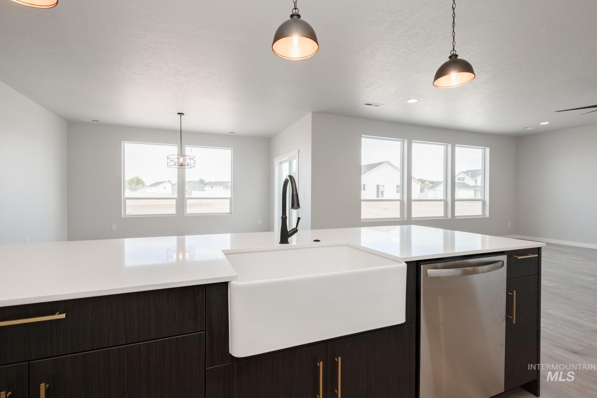 Kitchen with stainless steel dishwasher, hanging light fixtures, modern cabinets, light wood finished floors, and dark brown cabinetry