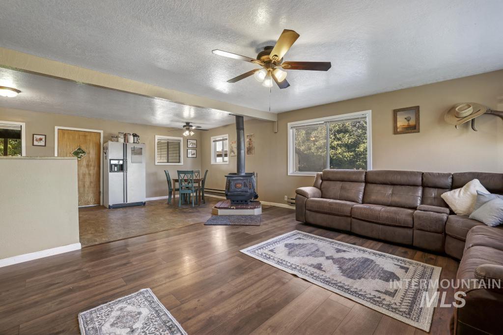 Living room with ceiling fan, a wood stove, a textured ceiling, and dark wood finished floors