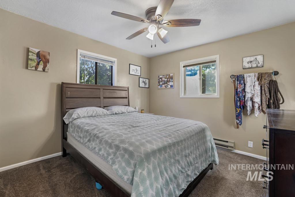 Bedroom with dark carpet, baseboard heating, and ceiling fan